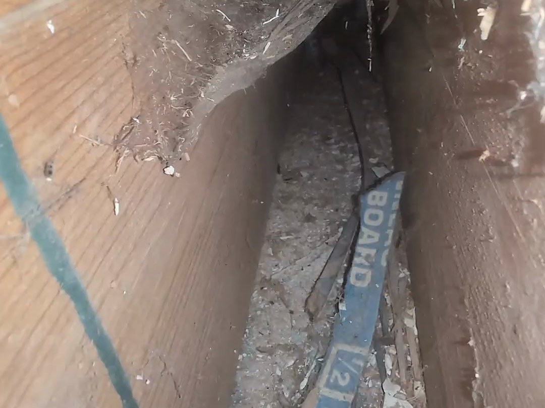 A duct channel between the joists packed with construction debris, loose nails and a scrap of board, before cleaning